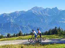 Due persone scendono in scooter alpino e sullo sfondo si intravedono le montagne della Bündner Herrschaft