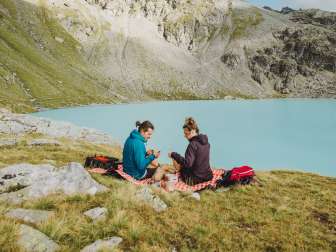 Coppia seduta su una coperta da picnic davanti a un lago di montagna blu ghiaccio