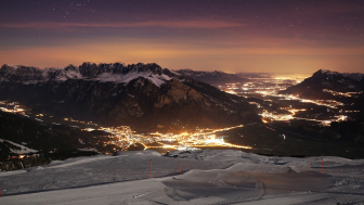 Vista del Sarganserland invernale di notte. In primo piano si vede una pista da sci. Nella valle si vedono le luci colorate.