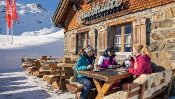 Tre amici si godono un caffè sulla terrazza soleggiata della Gruebhütte