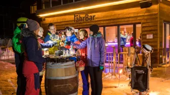 Un gruppo di appassionati di sport invernali si trova davanti al FahrBar innevato e sorseggia bicchieri di vino.