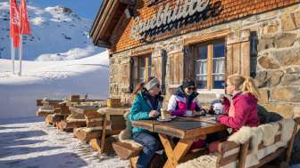 Tre amici si godono un caffè sulla terrazza soleggiata della Gruebhütte